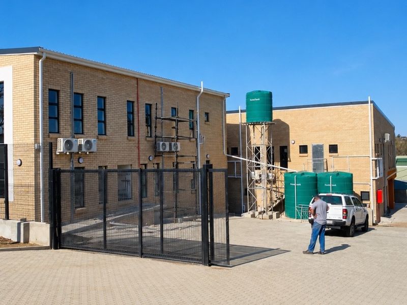 Rear exterior view of a brick office building featuring a paved parking area, security fencing, and external water storage tanks.