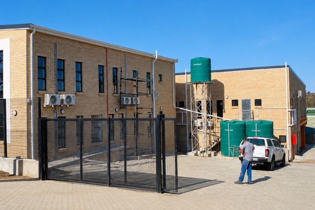 Rear exterior view of a brick office building featuring a paved parking area, security fencing, and external water storage tanks.