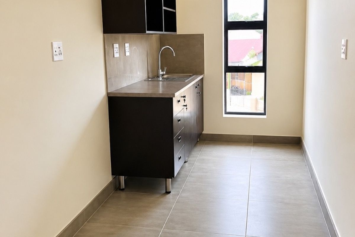A clean, modern kitchenette featuring dark cabinetry, a stainless steel sink, tiled flooring, and a neutral color palette in an office setting.