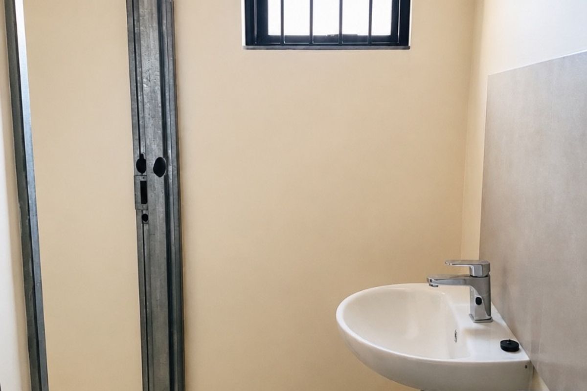 A functional bathroom space featuring double vanity basins with chrome mixer taps and a window fitted with a security gate.