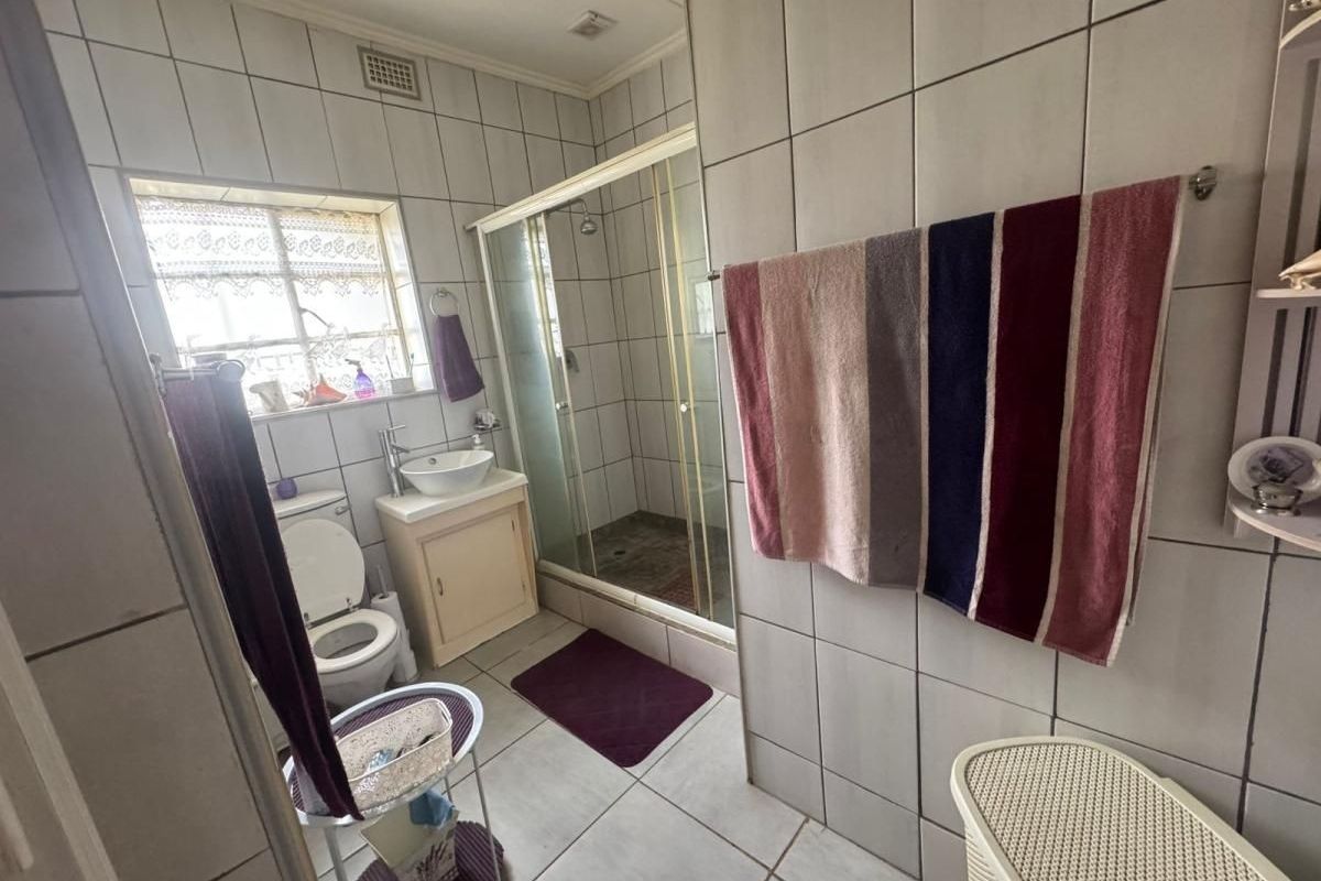 A functional bathroom featuring a shower enclosure, vanity cabinet with vessel sink, and full-height wall tiling.