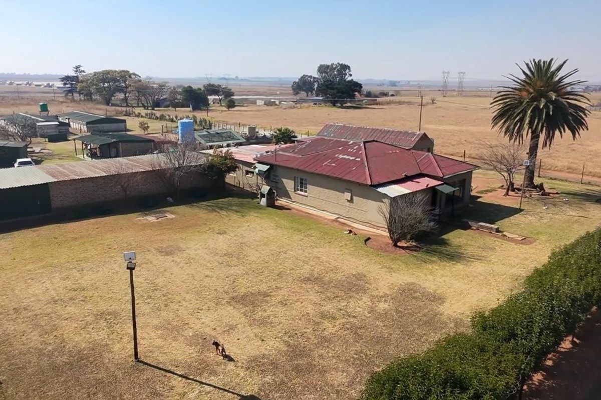 Aerial view of a farm property featuring a main residence with a corrugated metal roof, surrounding outbuildings, and expansive open land.