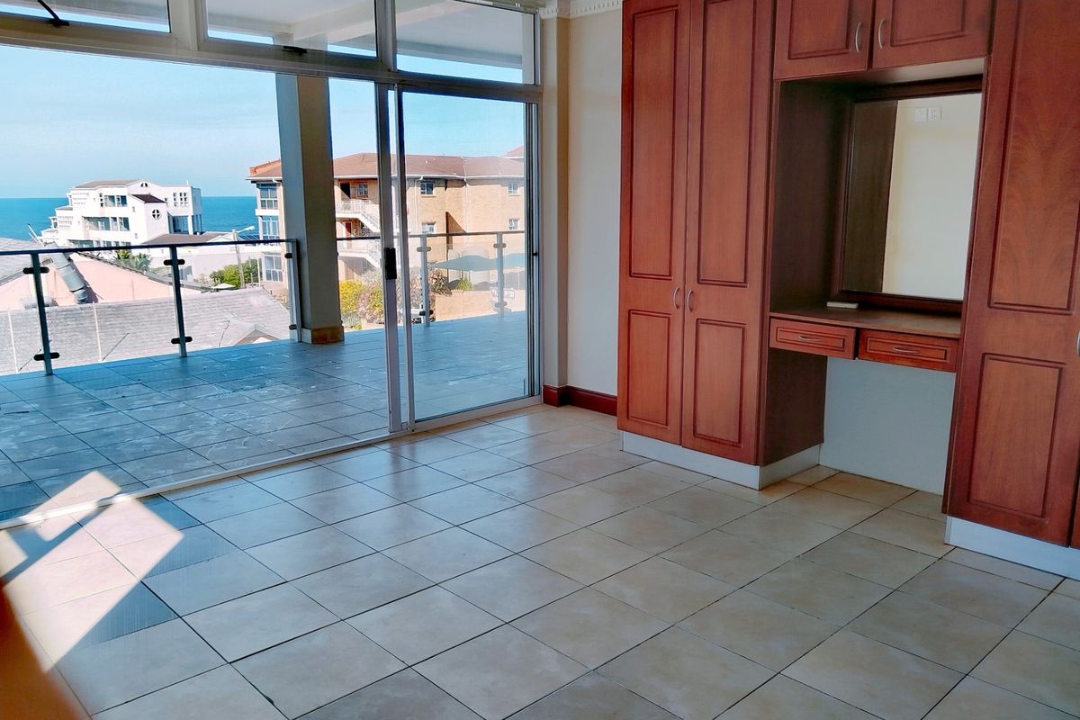 Spacious bedroom featuring built-in cabinetry, vanity unit, and large sliding glass doors opening onto a balcony with coastal views.