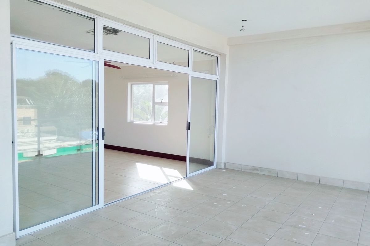 An empty, open-plan living area featuring large sliding glass doors, neutral tiled flooring, and clean white walls, ready for personalization.