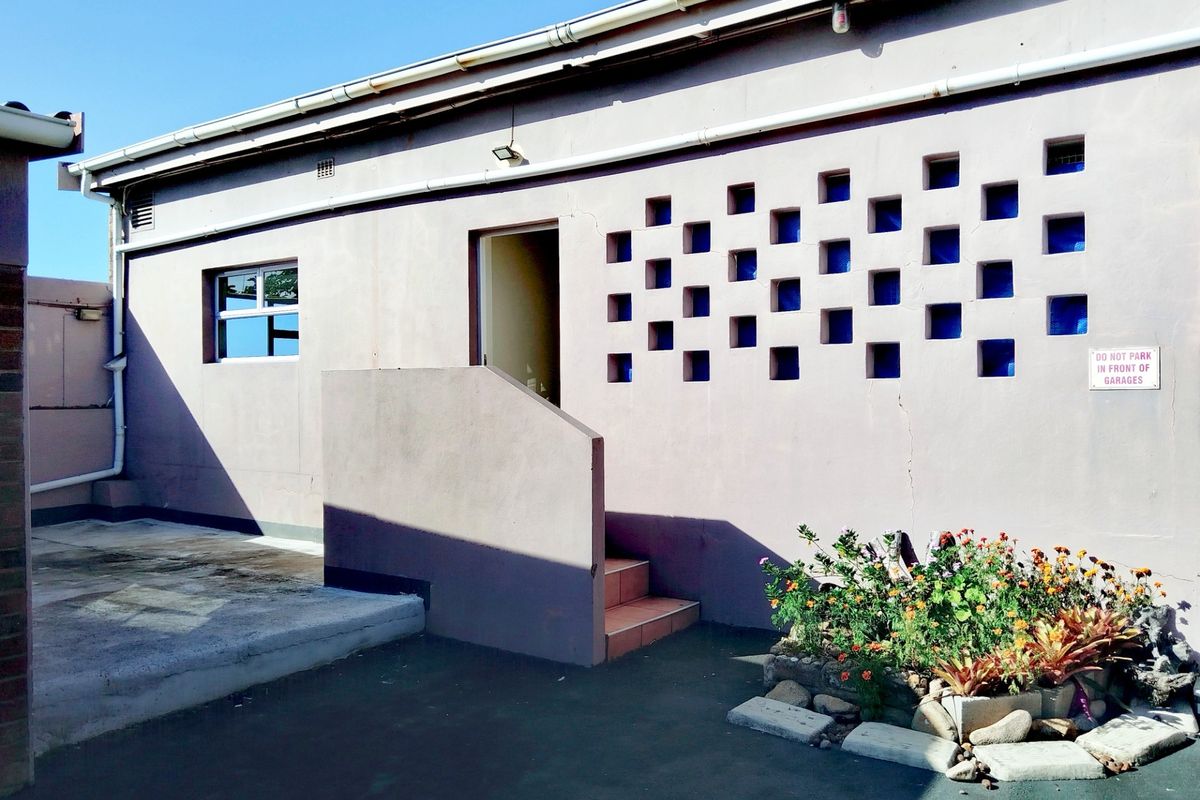Rear exterior view of the apartment building featuring a concrete staircase, decorative block wall detailing, and paved outdoor area.