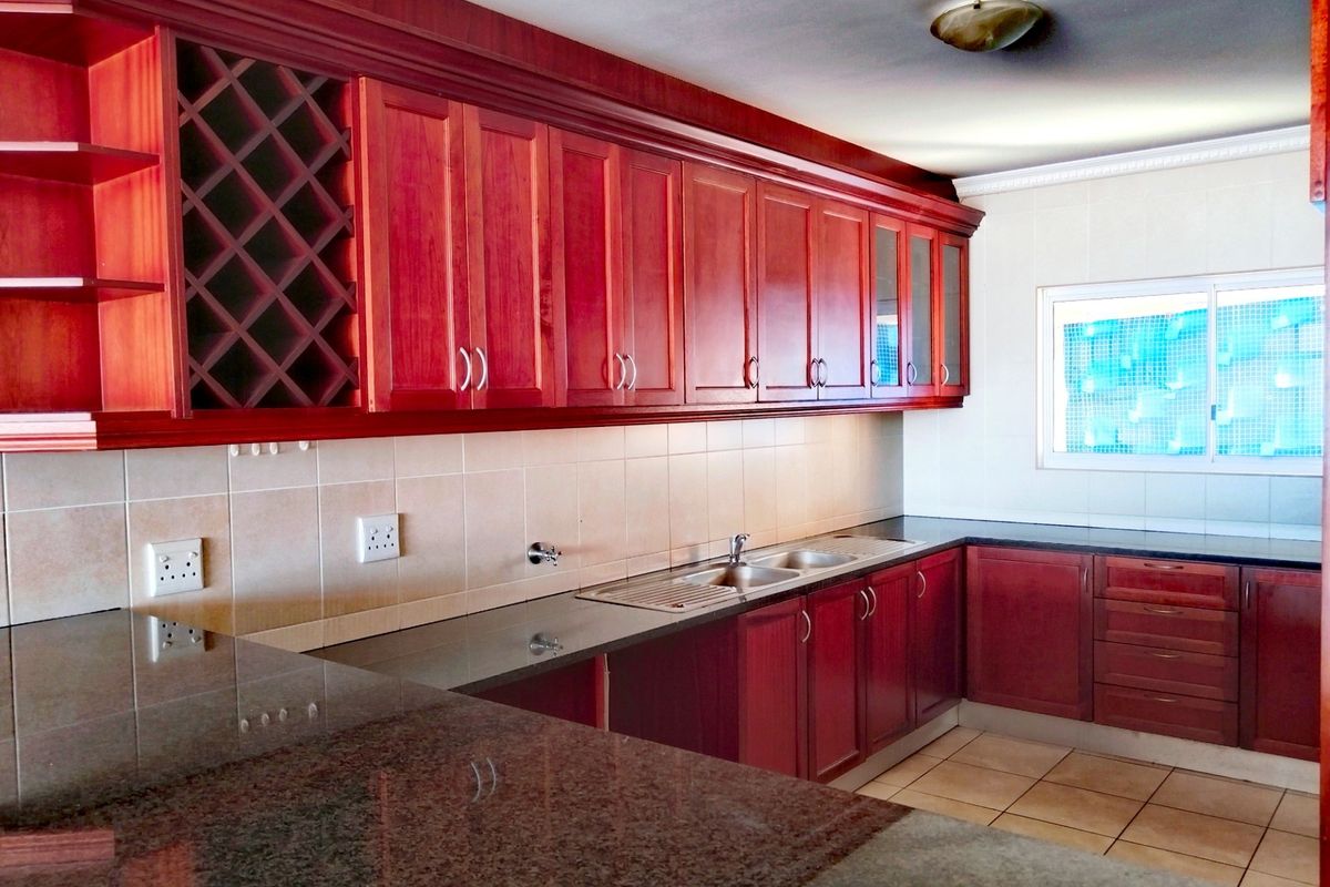 A spacious kitchen featuring dark wood cabinetry, granite countertops, a double sink, and a tiled backsplash, offering a functional layout for culinary activities.