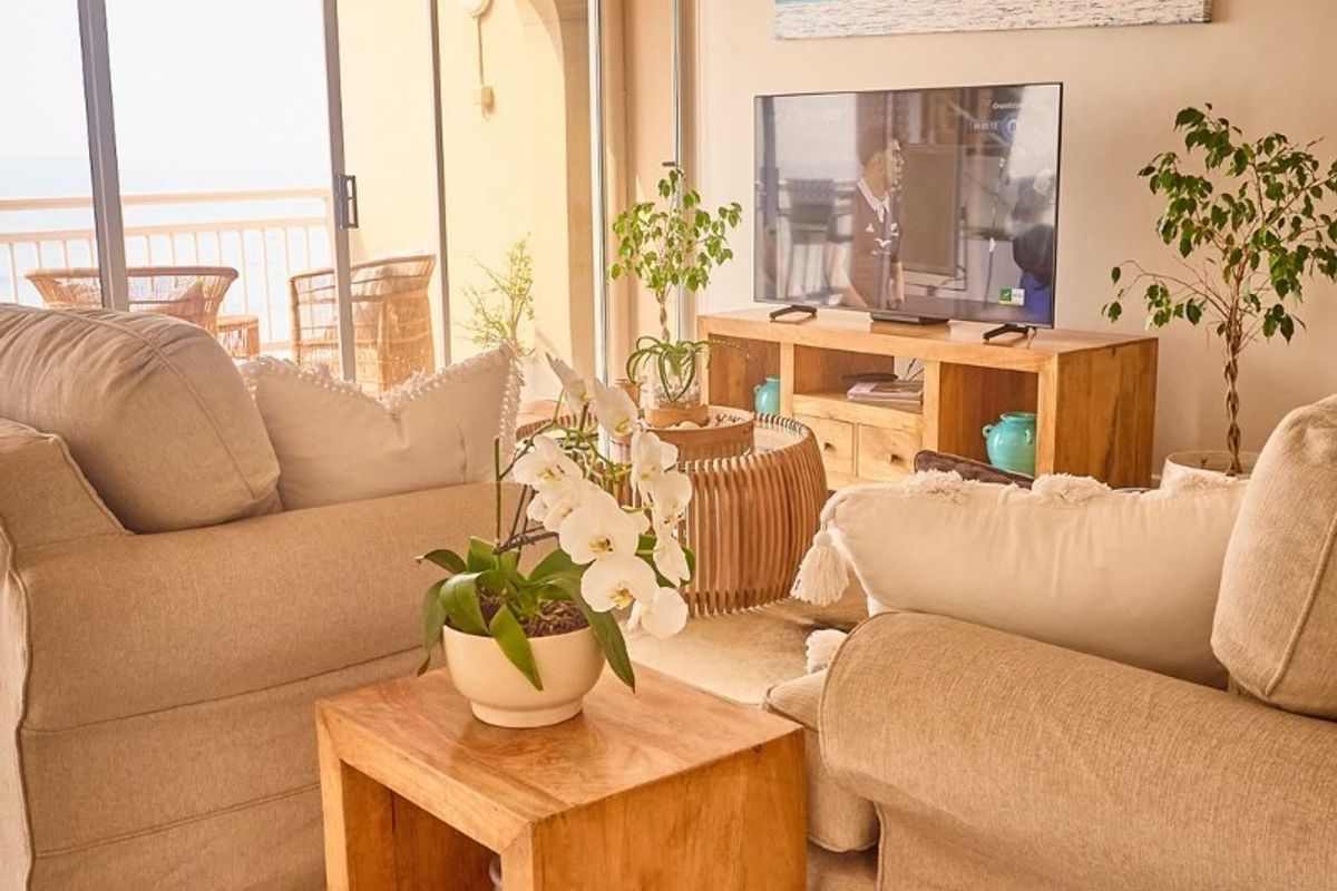 A bright and airy living room featuring concrete flooring, recessed ceiling lighting, and large sliding glass doors that open onto a balcony.