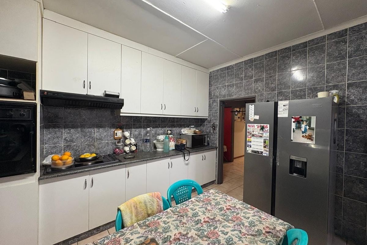 Functional kitchen featuring white cabinetry, dark tiled backsplash, built-in oven, and hob, with tiled flooring throughout.