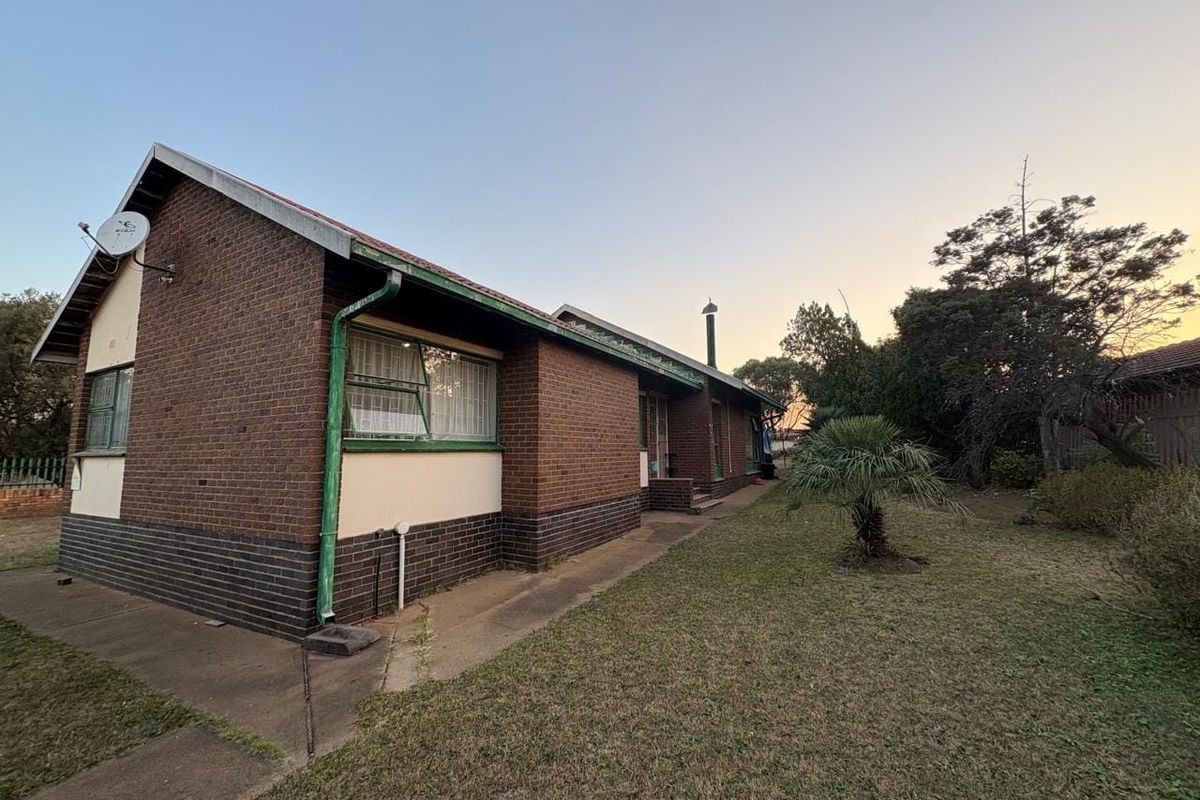 Rear view of a brick house featuring a concrete pathway, established garden area, and exterior chimney flue.