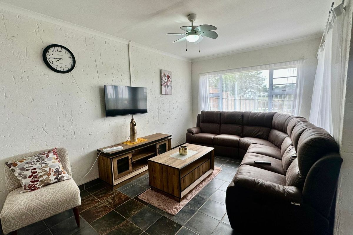 A comfortable living room featuring tiled flooring, a ceiling fan, and a large window providing natural light.