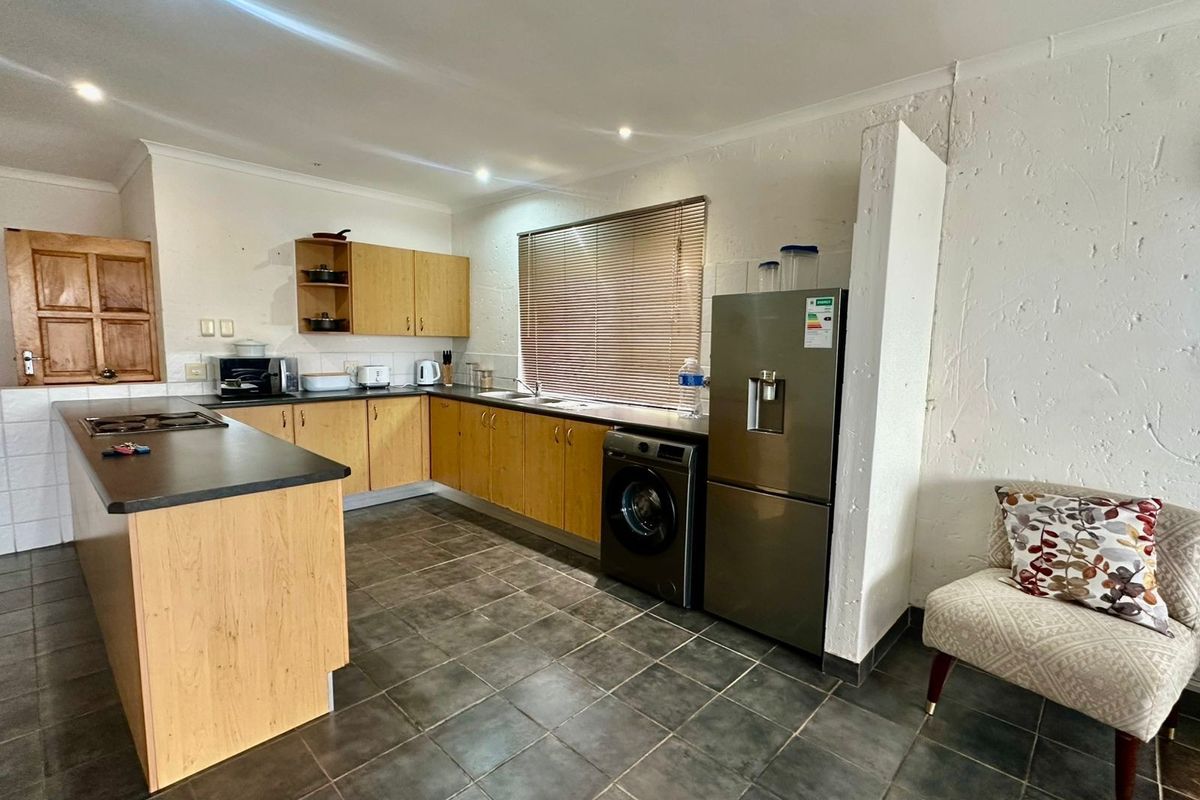 Functional kitchen featuring light wood cabinetry, dark laminate countertops, tiled flooring, and integrated hob, with a practical layout and neutral finishes.