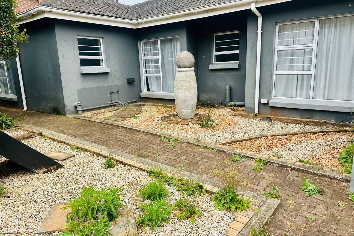 Rear exterior view of the property featuring a paved walkway, gravel garden beds, and a tiled roof structure requiring maintenance.