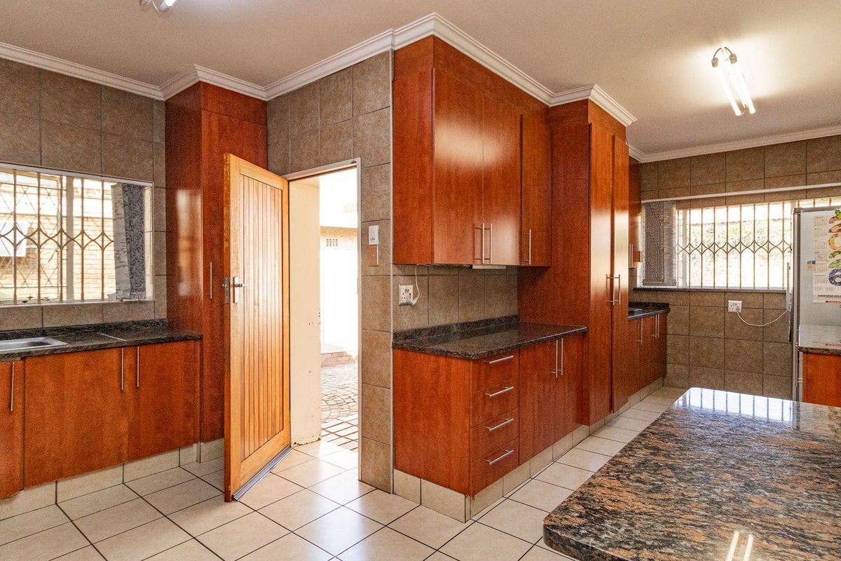 A functional kitchen featuring extensive wooden cabinetry, granite countertops, tiled splashbacks, and direct access to an outdoor area.