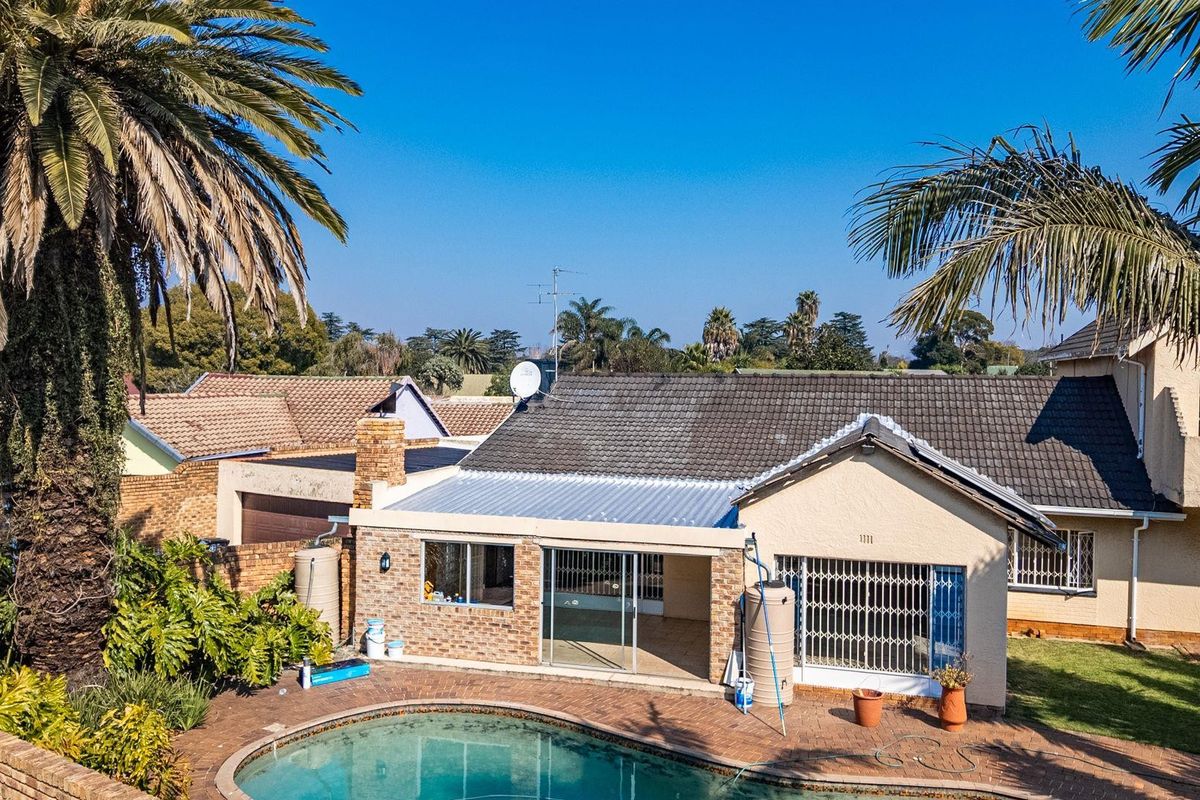 Aerial view of the rear exterior featuring a swimming pool, brick paved patio area, and a single-story house with a tiled roof.