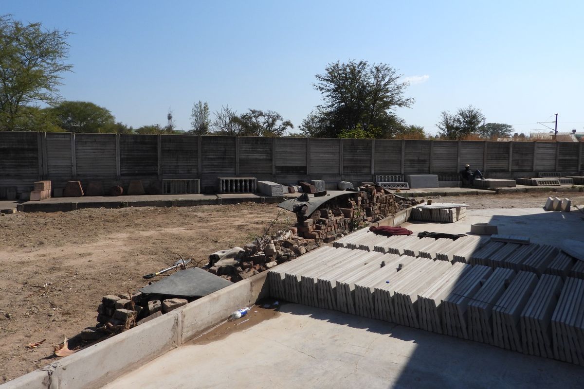 Rear yard area featuring a precast concrete boundary wall and concrete slab, currently used for storage of building materials and construction supplies.