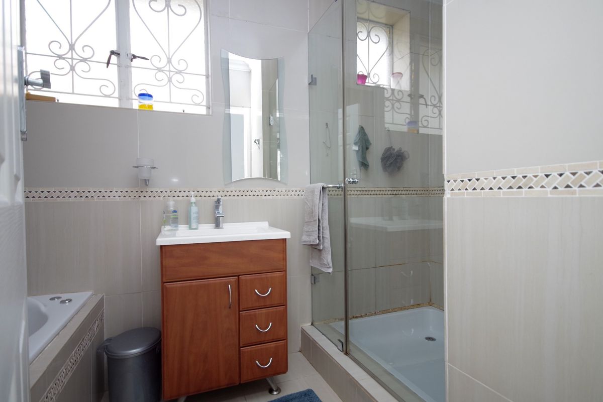 A functional bathroom featuring a vanity cabinet, a built-in bathtub, and a separate glass-enclosed shower with neutral wall tiling.