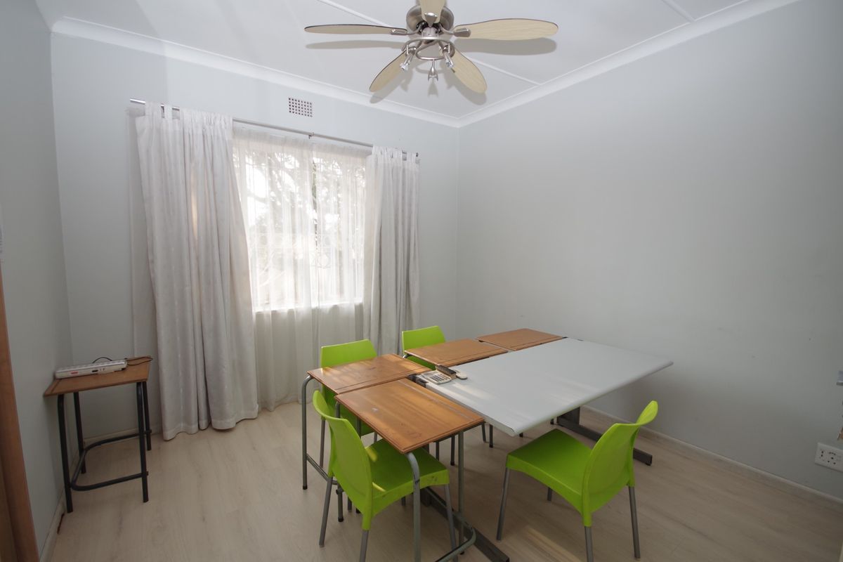 A functional bedroom featuring light-toned laminate flooring, a ceiling fan, and neutral wall finishes, suitable for use as a bedroom or home office.