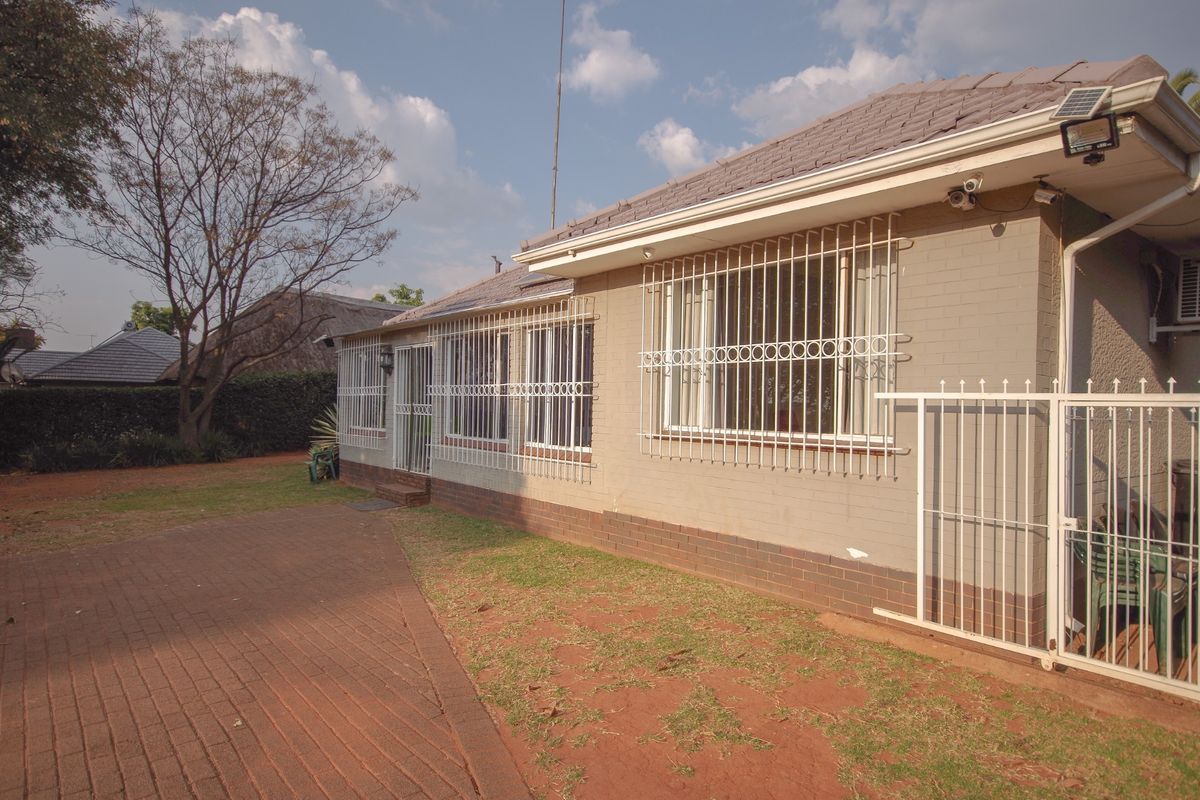 Rear exterior view of the house featuring brick walls, security bars on windows, a paved driveway, and a tiled roof.