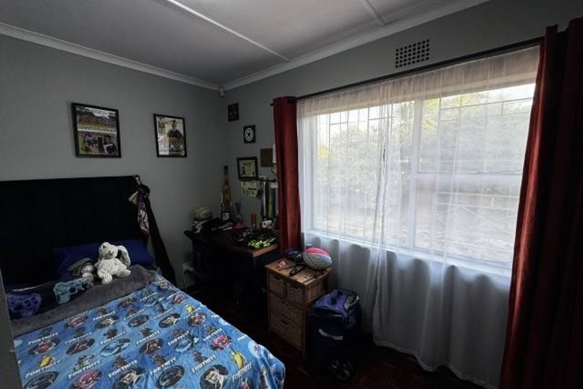A bedroom featuring parquet flooring, a large window with security bars, and classic cornice detailing.