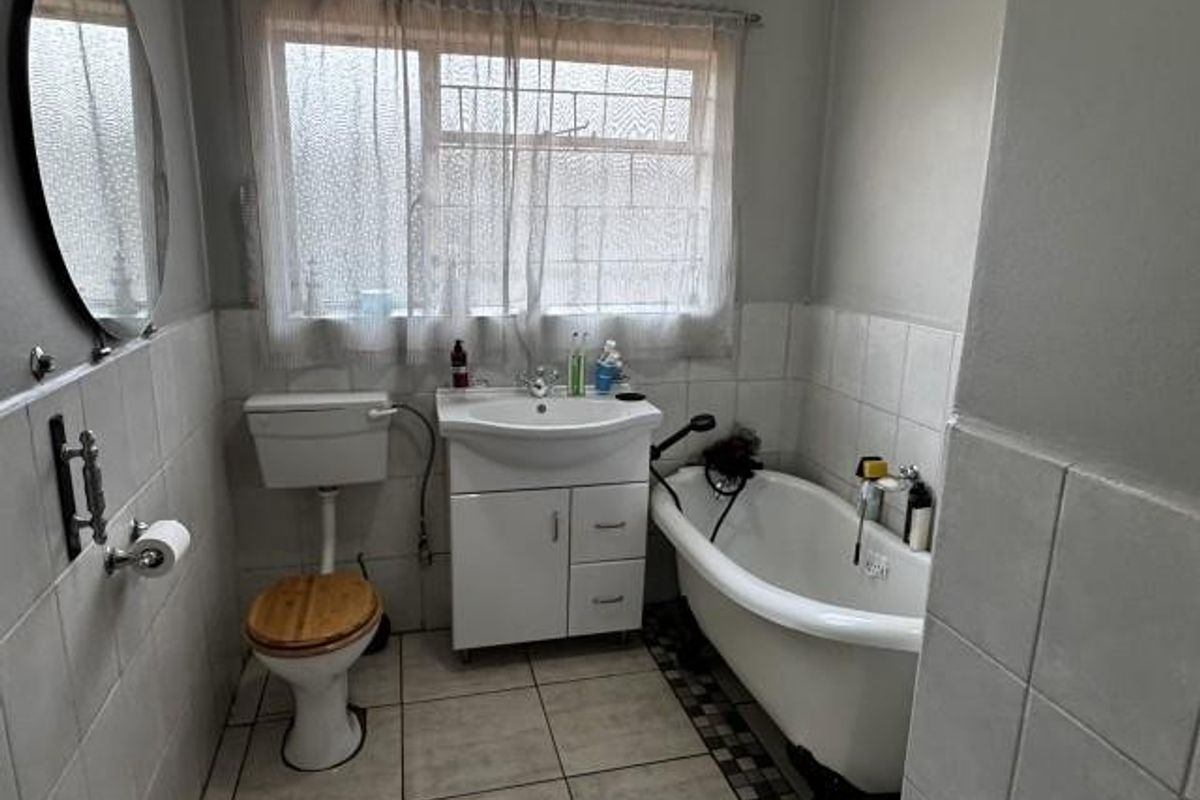 A functional bathroom featuring a classic clawfoot bathtub, pedestal vanity, and tiled finishes, offering a traditional aesthetic with potential for modernization.