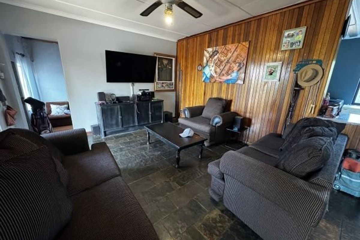 A living room featuring dark stone tile flooring, a ceiling fan, and a prominent wood-paneled feature wall.