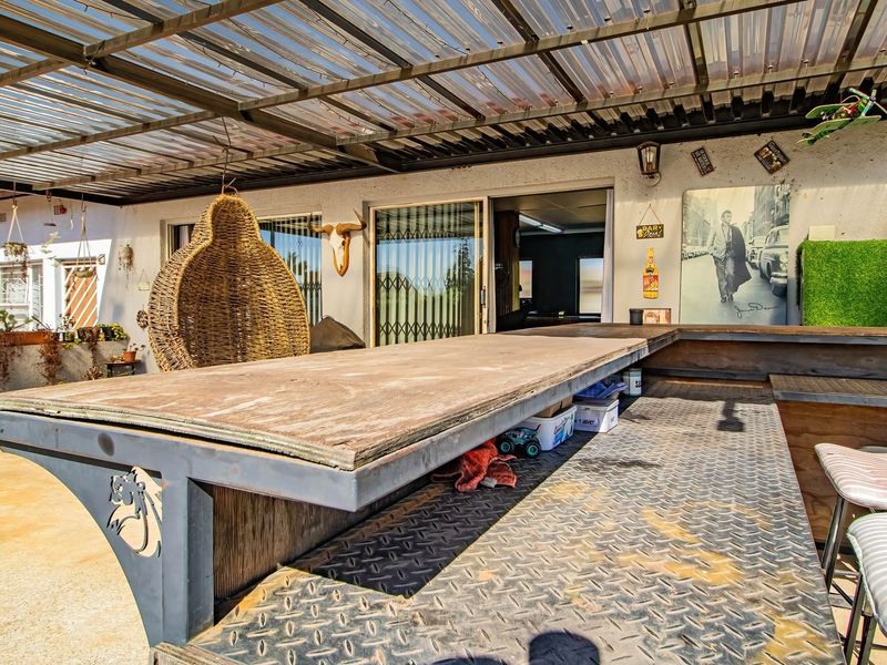 Covered outdoor patio area featuring a built-in bar with metal diamond plate detailing and a corrugated roof structure.