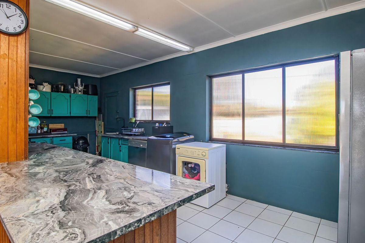 A functional kitchen featuring marble-look countertops, teal cabinetry, and tiled flooring, offering a practical layout with ample natural light from sliding windows.