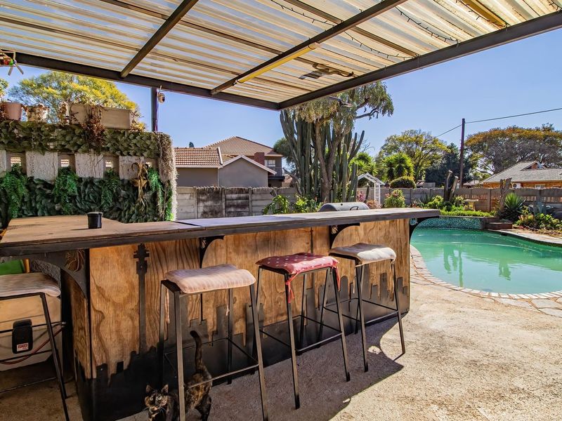 Outdoor entertainment area featuring a covered patio with a built-in bar overlooking a swimming pool and garden.