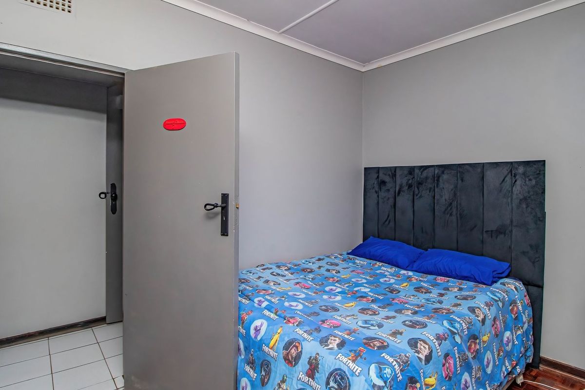 A bedroom featuring a mix of tiled and wooden flooring, neutral wall finishes, and a built-in headboard.