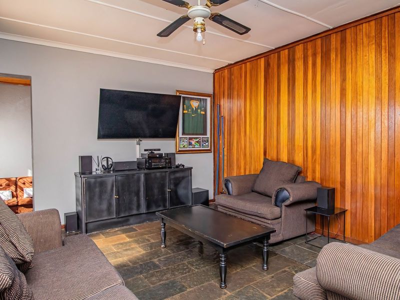 A living room featuring wood paneling, stone tile flooring, and a ceiling fan, offering a classic, dated aesthetic ready for modernization.