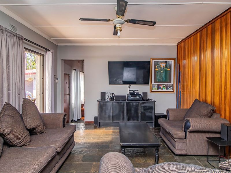 A living room featuring slate tile flooring, wood paneling on one wall, and a ceiling fan, with access to an outdoor area via sliding doors.