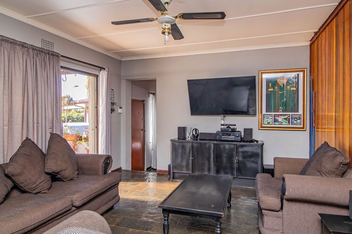 A living room featuring stone tile flooring, a ceiling fan, and a wood-paneled accent wall with direct access to an outdoor area.