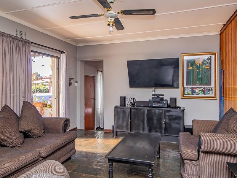 A living room featuring stone tile flooring, a ceiling fan, and a wood-paneled accent wall with direct access to an outdoor area.