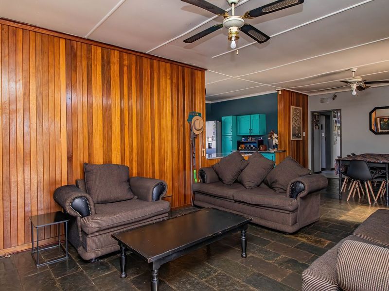 Open-plan living and dining area featuring timber wall paneling, slate tile flooring, and ceiling fans, with an adjacent kitchen space.