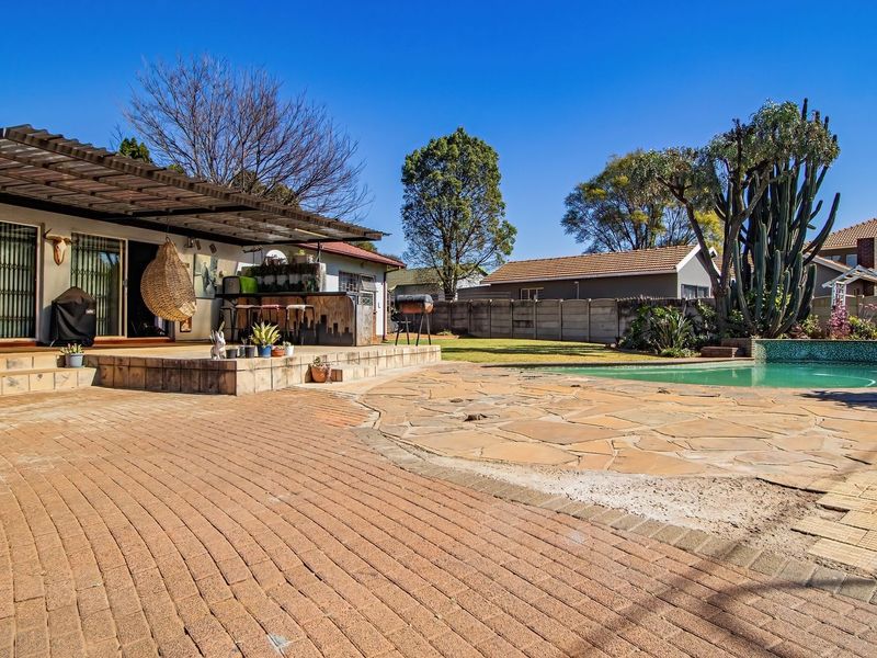 Spacious rear garden featuring a swimming pool, a large paved terrace, and a covered patio area with a built-in bar counter.