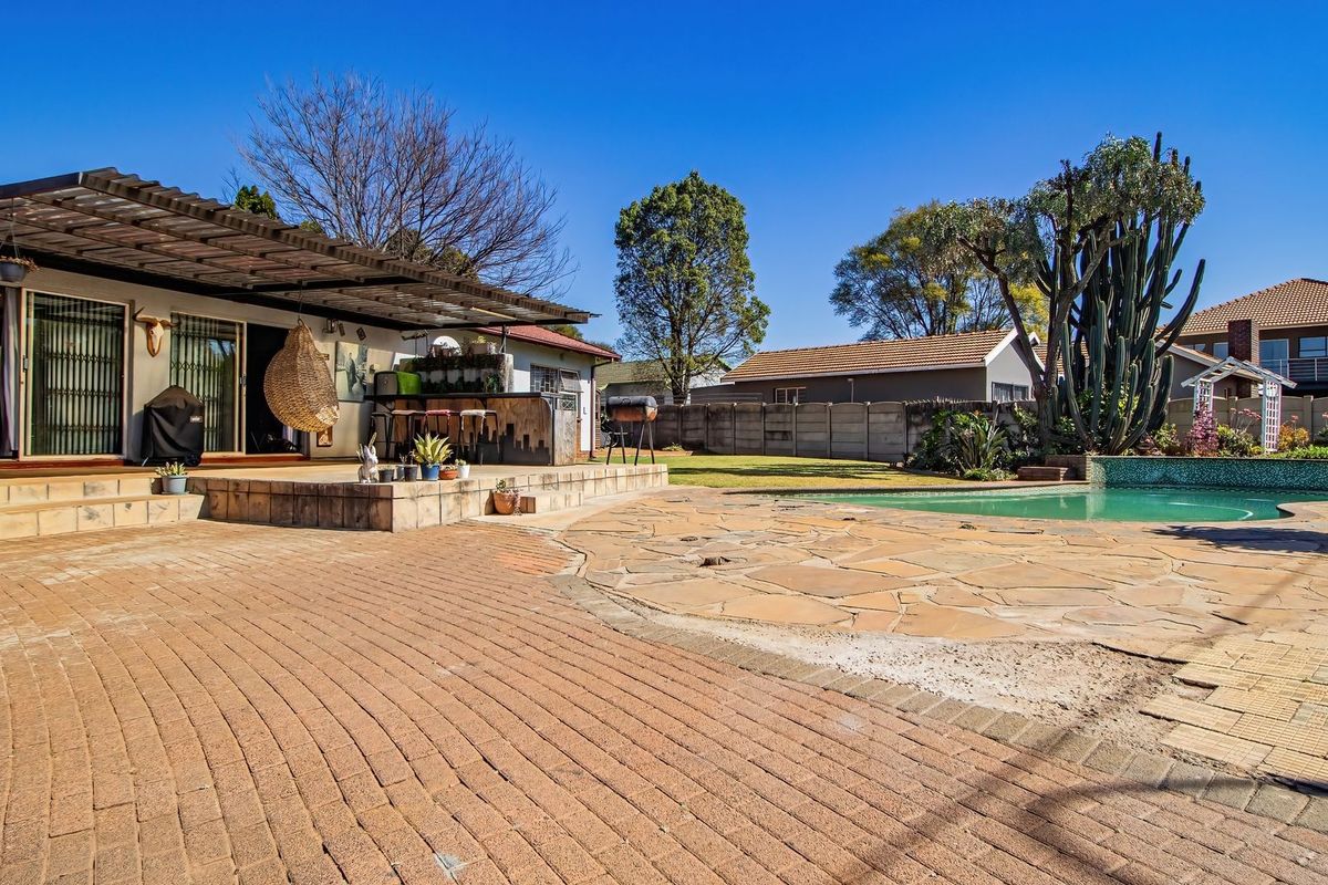 Spacious rear garden featuring a swimming pool, a large paved terrace, and a covered patio area with a built-in bar counter.