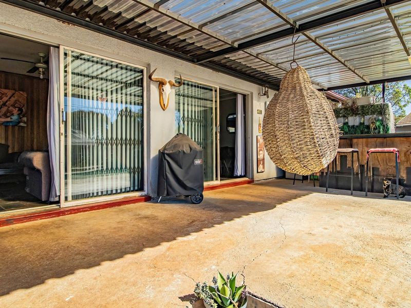 Covered outdoor patio area featuring concrete flooring, sliding glass door access to the interior, and a corrugated roof structure.