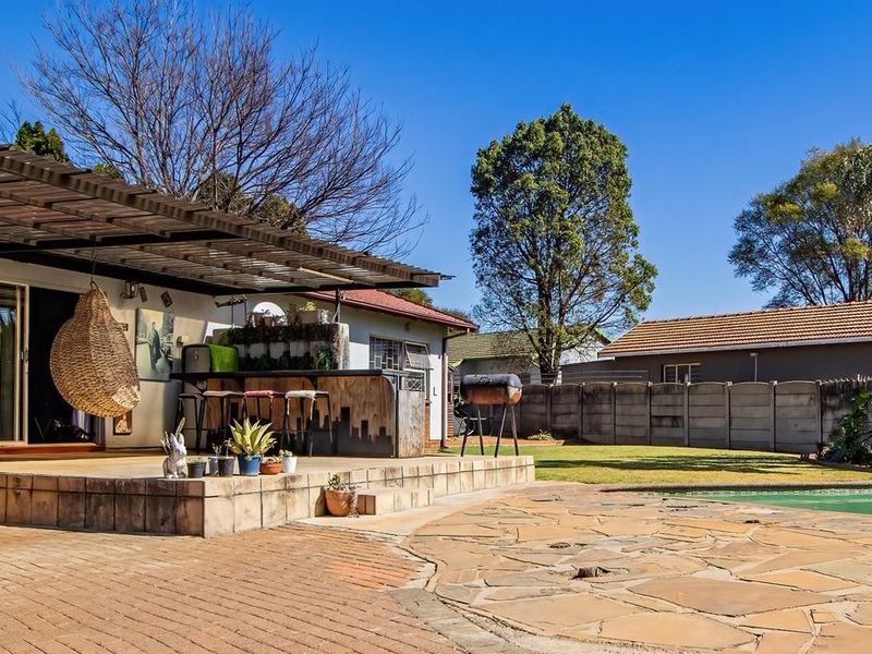 Spacious covered patio area featuring a built-in bar, overlooking a swimming pool and landscaped garden, ideal for outdoor entertaining.