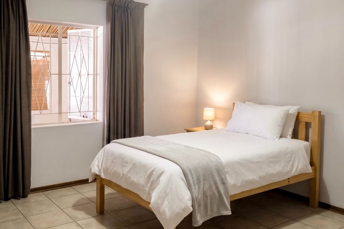 A clean and well-maintained bedroom featuring neutral tiled flooring, a security gate on the window, and full-length curtains.