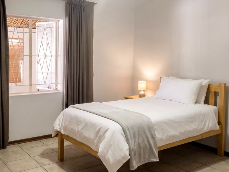 A clean and well-maintained bedroom featuring neutral tiled flooring, a security gate on the window, and full-length curtains.