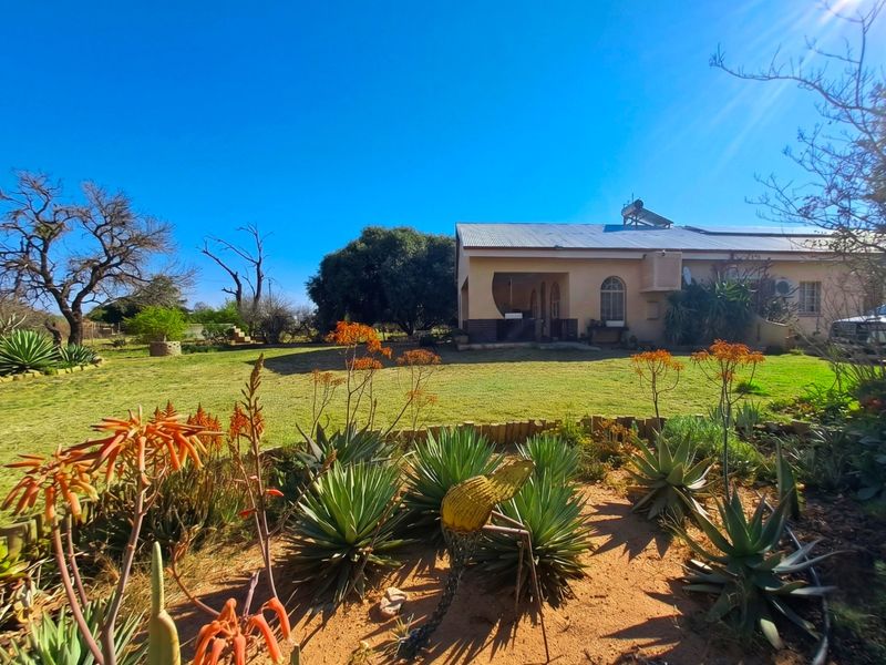 A view of the rear elevation of the property featuring a well-maintained garden, covered patio area, and solar water heating system on the roof.