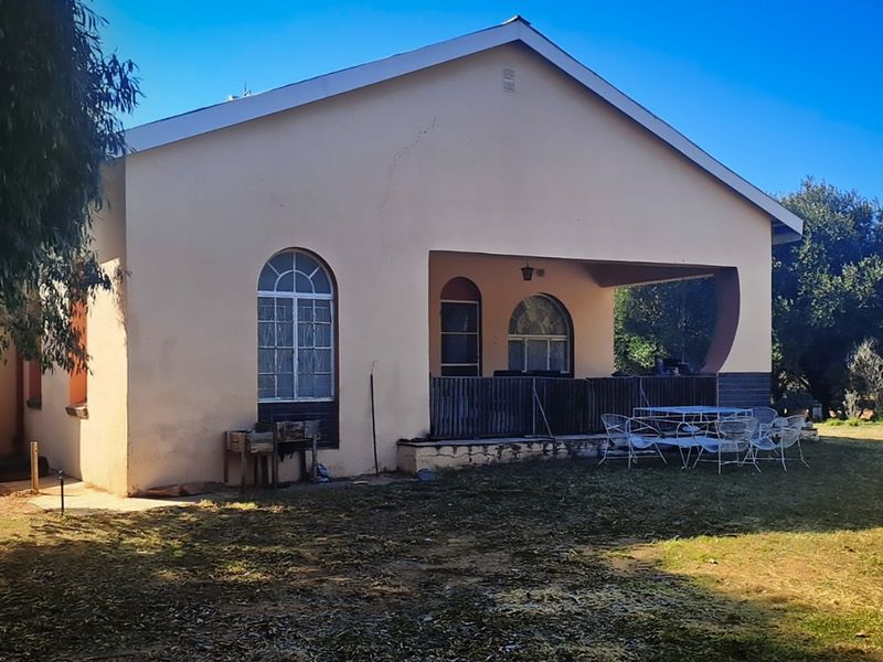 Rear view of the property featuring a covered patio area, arched windows, and a spacious garden setting.