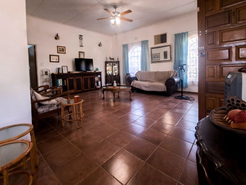 Spacious living room featuring large terracotta floor tiles, a central ceiling fan, and arched windows, offering a comfortable and traditional living space.