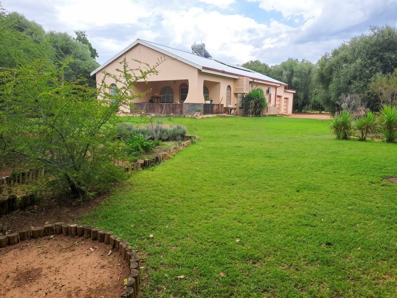 Rear view of a single-story residence featuring a covered patio, solar geyser, and expansive lawn area within a well-maintained garden setting.