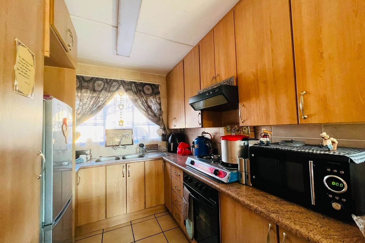 A functional galley-style kitchen featuring light wood-tone cabinetry, laminate countertops, a double sink, and built-in cooking appliances with tiled flooring throughout.