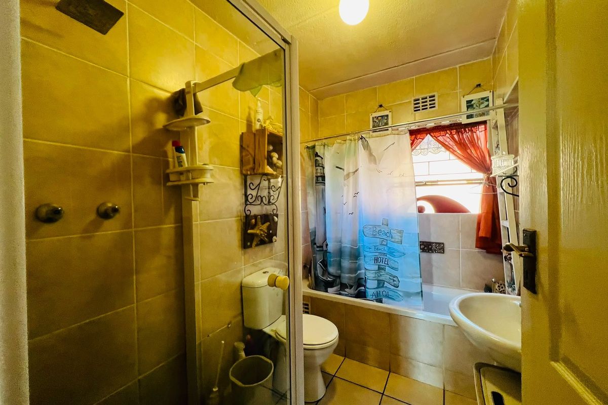 A compact bathroom featuring a combined shower and bathtub, pedestal basin, and toilet, finished with dated ceramic wall and floor tiling.
