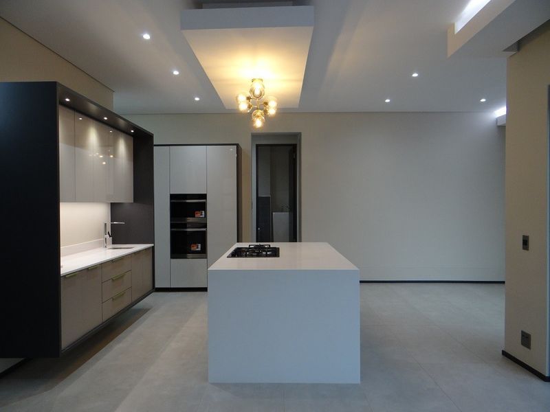 Modern, minimalist kitchen featuring a central island with a built-in cooktop, sleek cabinetry, integrated appliances, and recessed ceiling lighting in an open-plan layout.