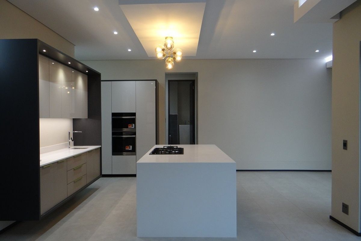 Modern, minimalist kitchen featuring a central island with a built-in cooktop, sleek cabinetry, integrated appliances, and recessed ceiling lighting in an open-plan layout.