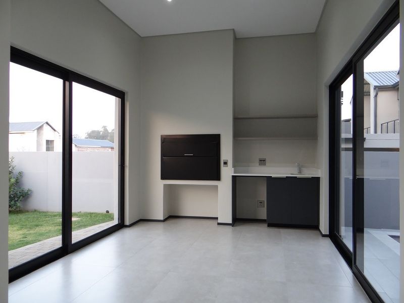 Modern covered patio featuring a built-in braai, sink, and sleek cabinetry, with large sliding glass doors opening to the garden.