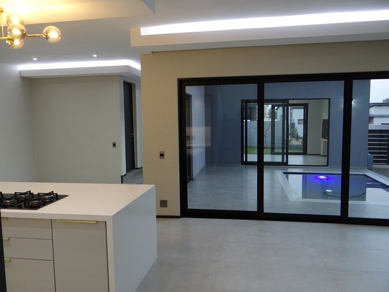 Modern open-plan living area featuring a sleek kitchen island with gas hob, recessed lighting, and large sliding doors opening to a private pool area.